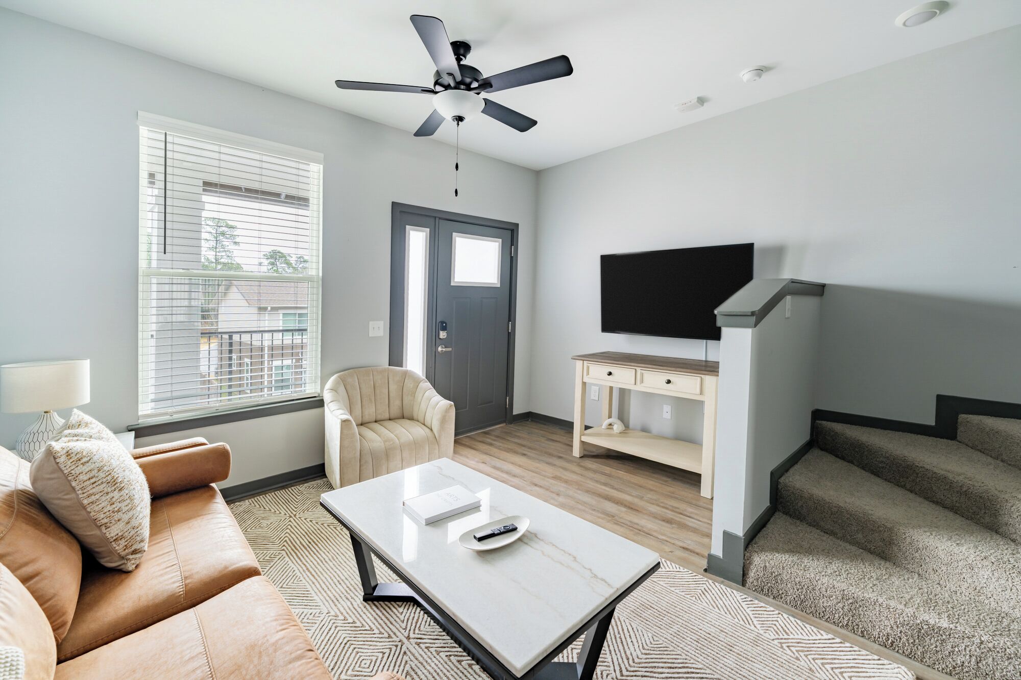 A modern living room with a sofa, coffee table, TV, and a ceiling fan.