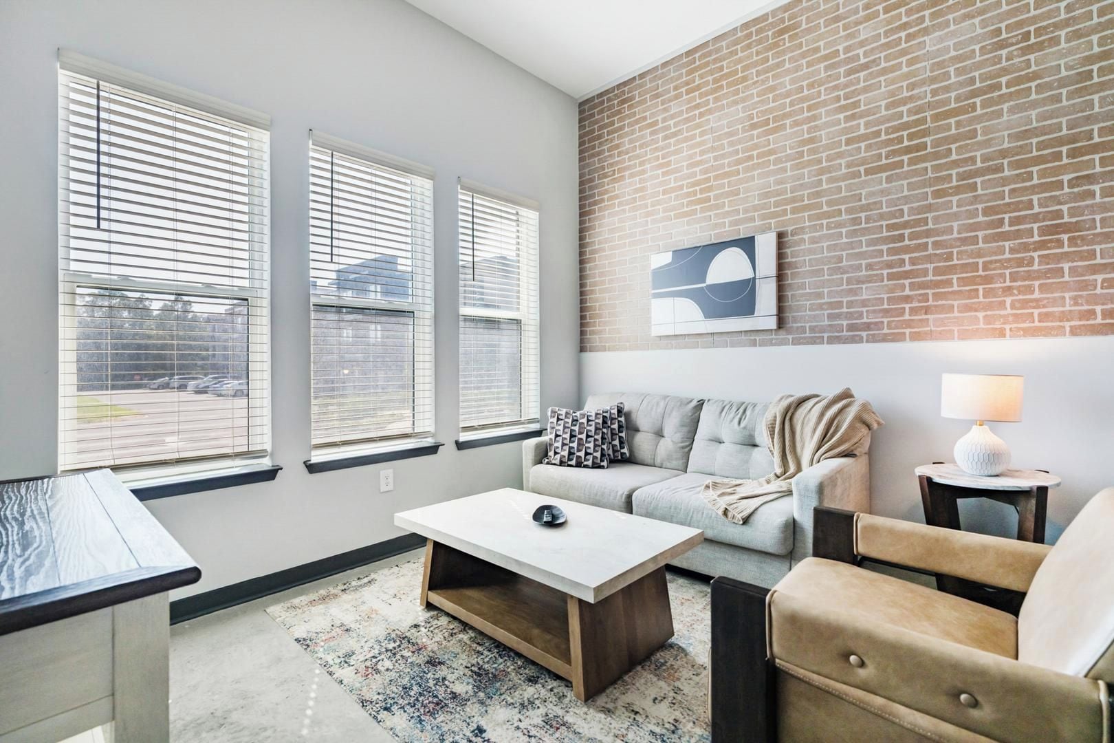 A modern living room with a brick accent wall, a grey sofa, a white coffee table, and a lamp.