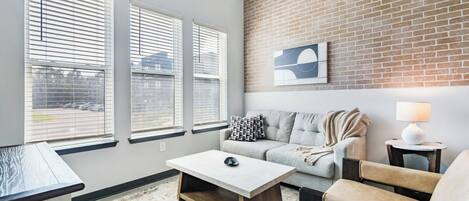A modern living room with a brick accent wall, a grey sofa, a white coffee table, and a lamp.