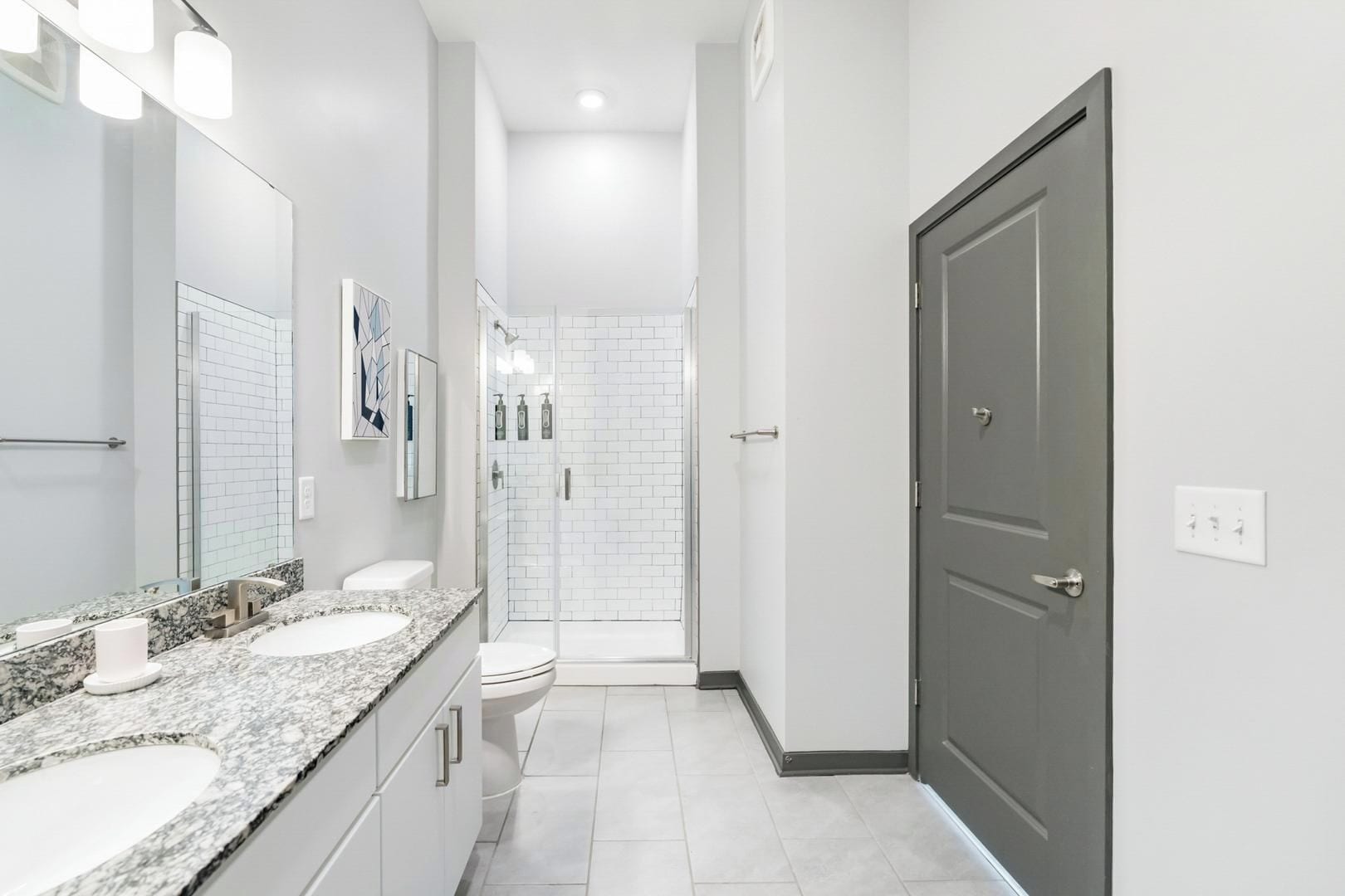 Une salle de bain moderne avec un meuble-lavabo à deux vasques, une douche en verre et une porte sombre.
