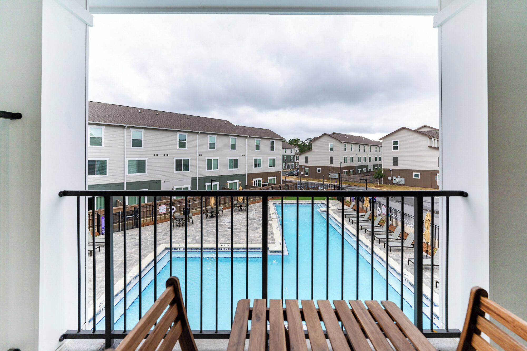 A balcony with a view of a swimming pool and adjacent buildings.
