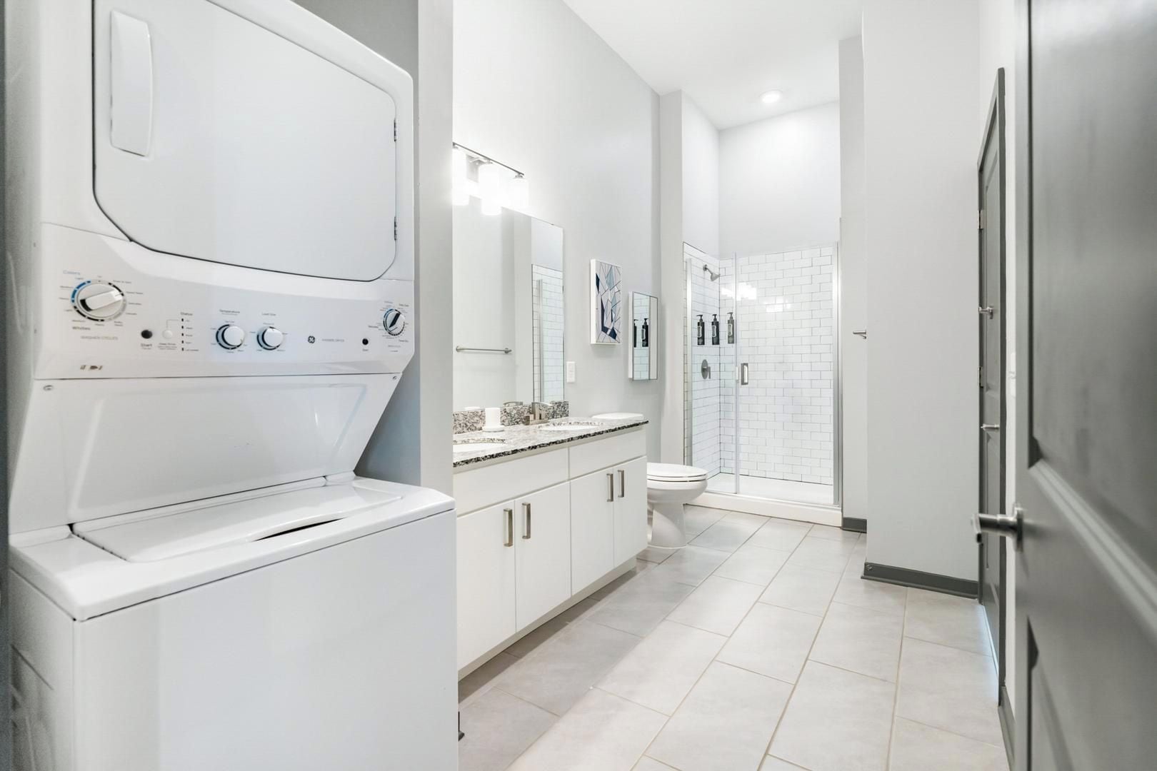 A modern bathroom with a built-in washer, a toilet, and a shower area.