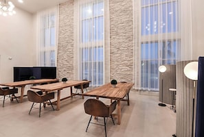 A modern hotel room with a large stone accent wall, a wooden dining table with chairs, a flat-screen TV, and a seating area with a sofa and a small table. - Landing Apartments - Northwest Pensacola (Pensacola)