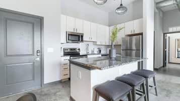 A modern kitchen with white cabinets, stainless steel appliances, a granite countertop, and bar stools.