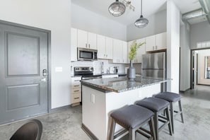A modern kitchen with white cabinets, stainless steel appliances, a granite countertop, and bar stools.