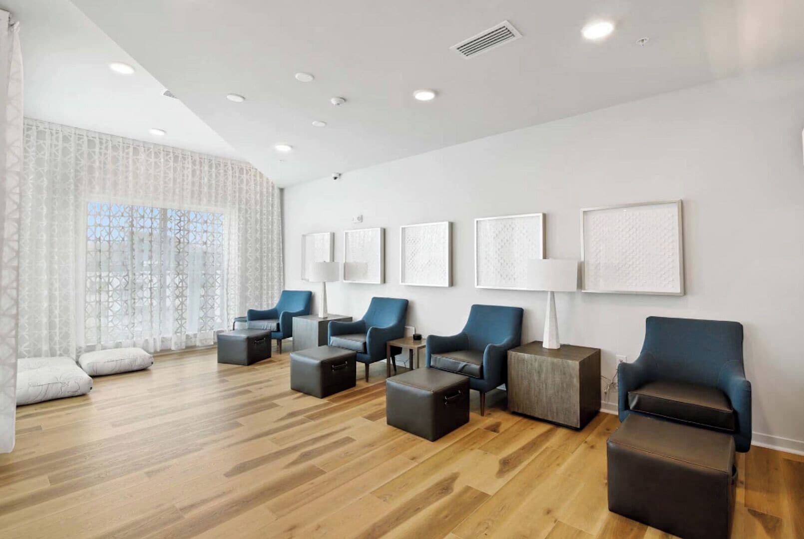 A modern hotel lobby with a wooden floor, blue armchairs, and a large window with sheer curtains.