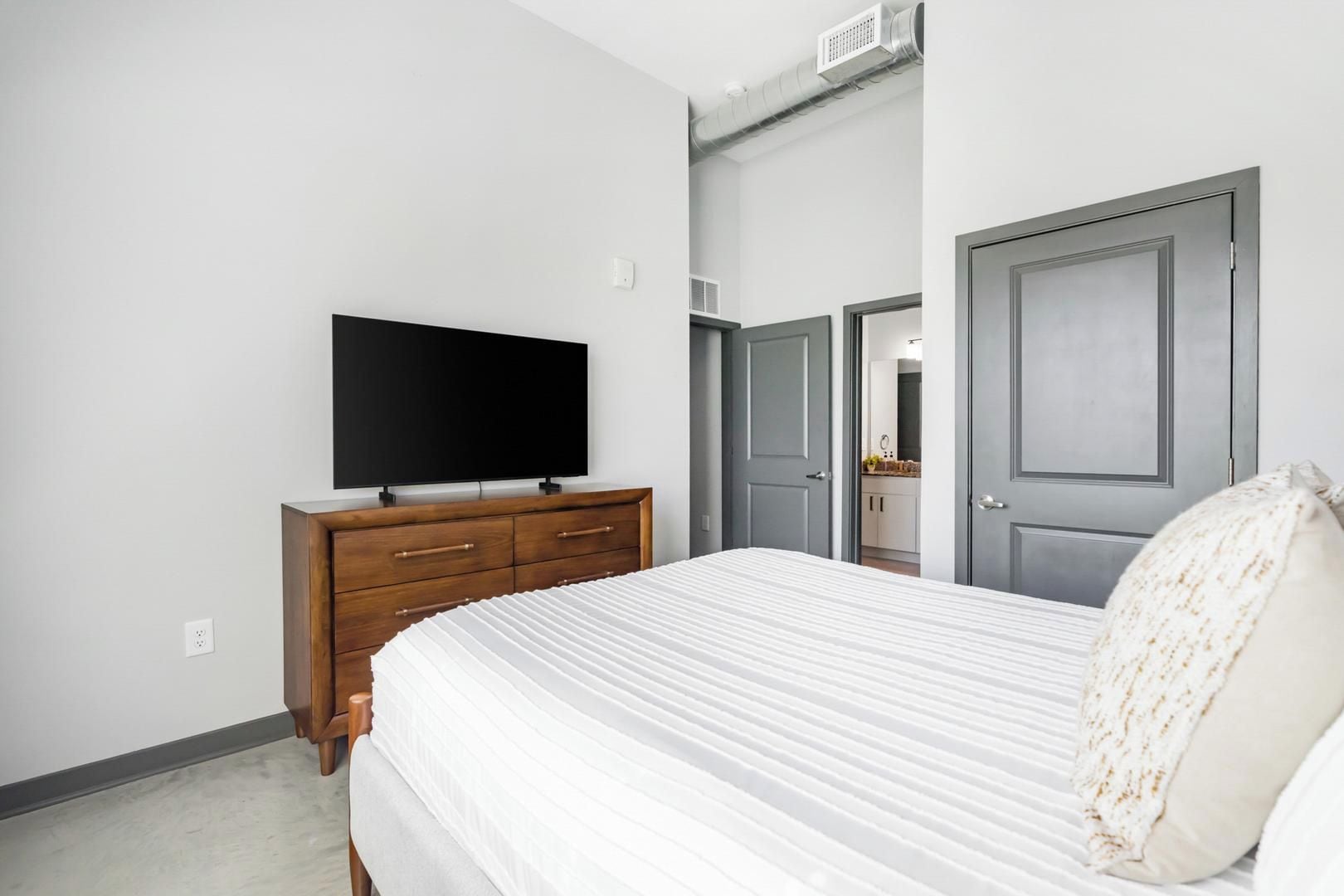 A bedroom with a bed, a dresser, a television, and a door to another room.