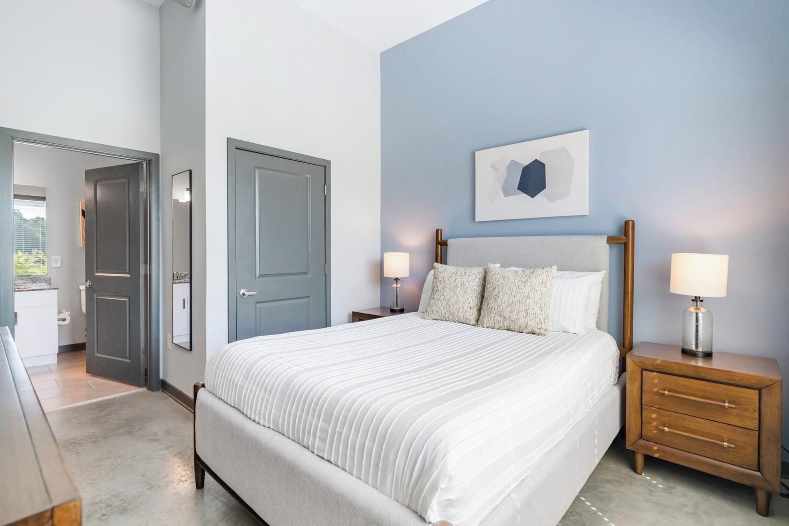 A bedroom with a bed, bedside tables, a door, and a wall-mounted artwork.