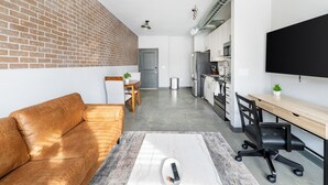 Un apartamento moderno con pared de ladrillo, sofá, comedor, cocina y televisor.