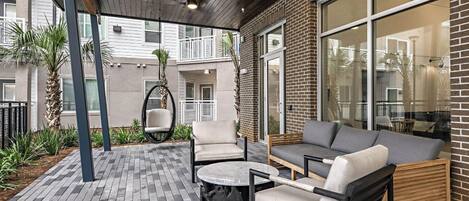 Un patio couvert avec un espace salon extérieur comprenant un canapé, des fauteuils et un fauteuil suspendu.
