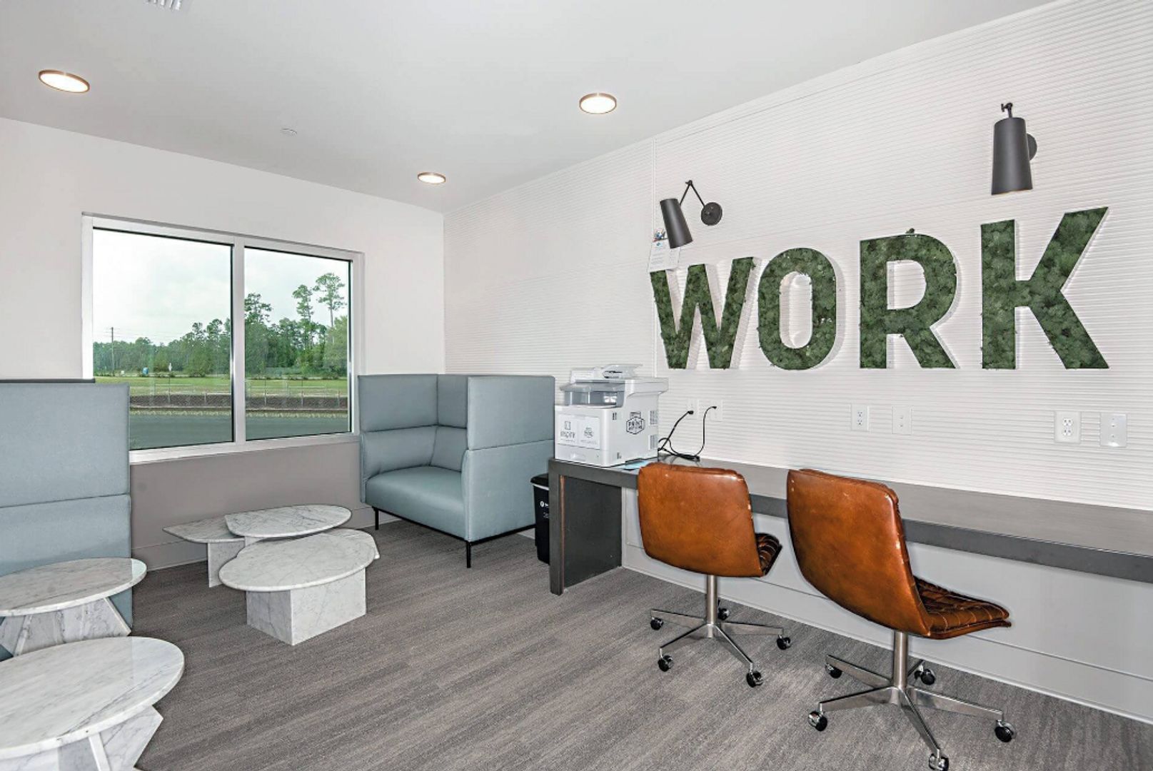 A modern office space with a large 'WORK' sign, grey and blue seating, and a view of the outdoors.