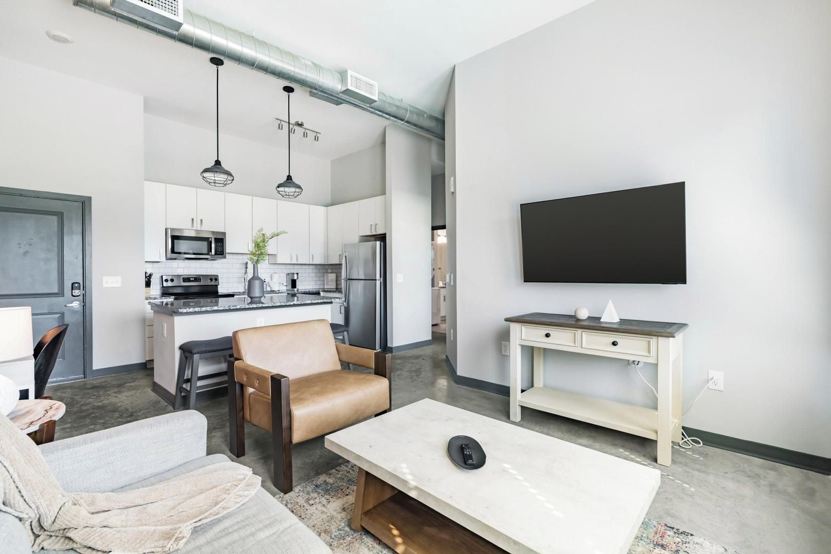 Ein modernes Wohnzimmer mit Küche, Essbereich, einer Sitzecke inklusive Sofa und Sessel sowie einem wandmontierten Flachbildfernseher.