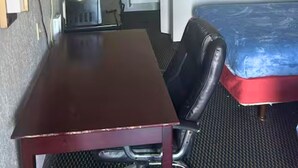 Une petite chambre d’hôtel avec un lit simple, un bureau, une chaise, un téléviseur et un tableau encadré au mur.