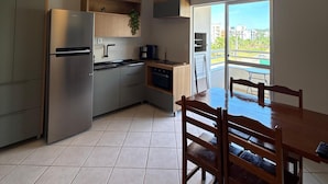 Een moderne keuken met een ingebouwde oven, een koelkast en een eethoek met een houten tafel en stoelen.