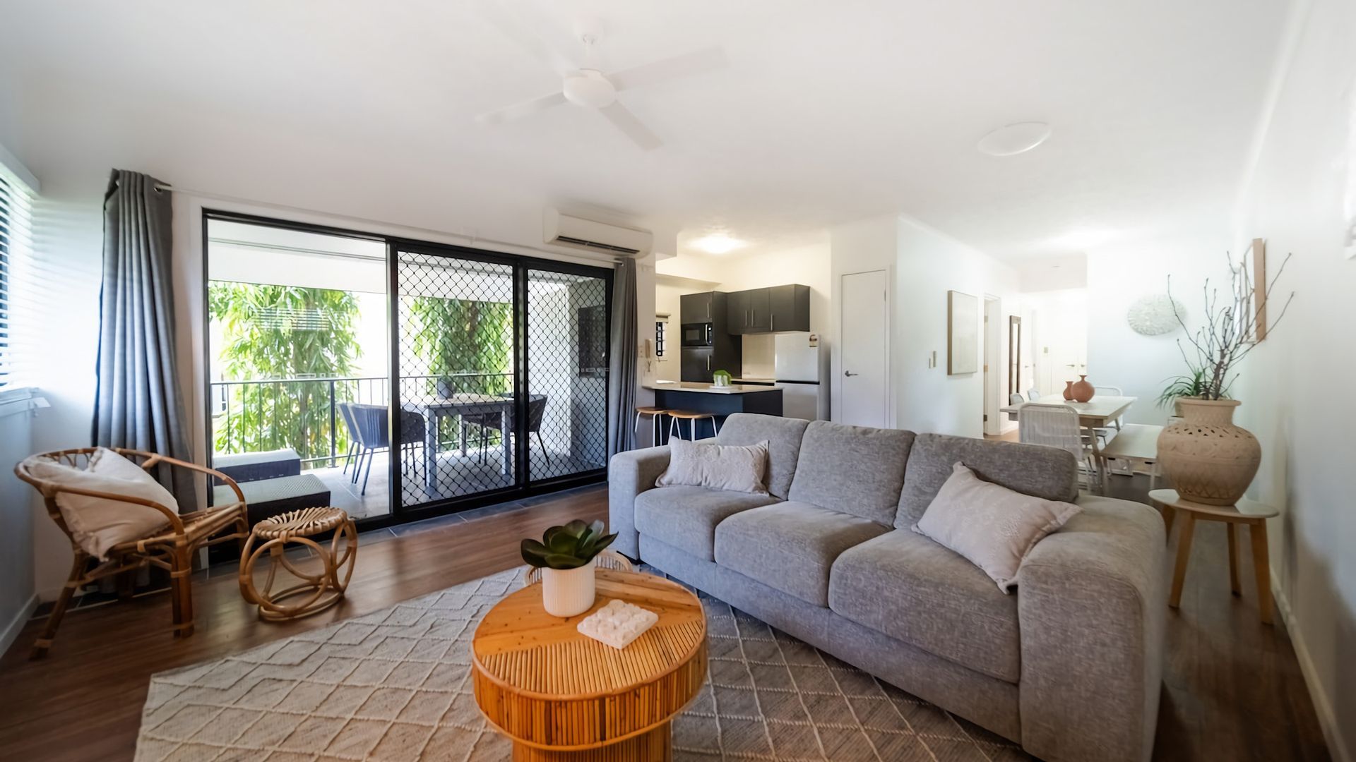 A modern living room with a sofa, a dining table, and a kitchen area visible through a sliding glass door.