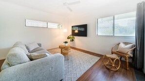 A living room with a grey sofa, a wicker chair, a small round table with a plant, and a ceiling fan. - North Ward Coastal Retreat Near The Strand (North Ward)