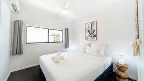 Ein Hotelzimmer mit einem Bett, einem Deckenventilator, einem Fenster mit Vorhängen und einem Wandbild.