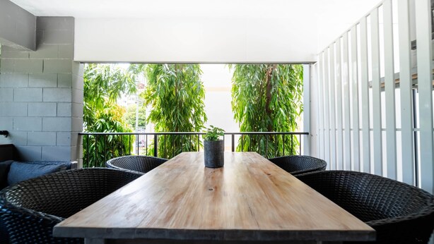 A wooden table with four chairs, a potted plant, and a view of greenery through a white railing. - North Ward Coastal Retreat Near The Strand (North Ward)
