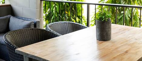 A wooden table with a potted plant, wicker chairs, and a balcony with greenery.
