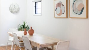 A dining area with a wooden table, white chairs, a potted plant, and abstract art on the wall. - North Ward Coastal Retreat Near The Strand (North Ward)