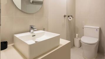 A modern bathroom with a white sink, mirror, toilet, and shower.