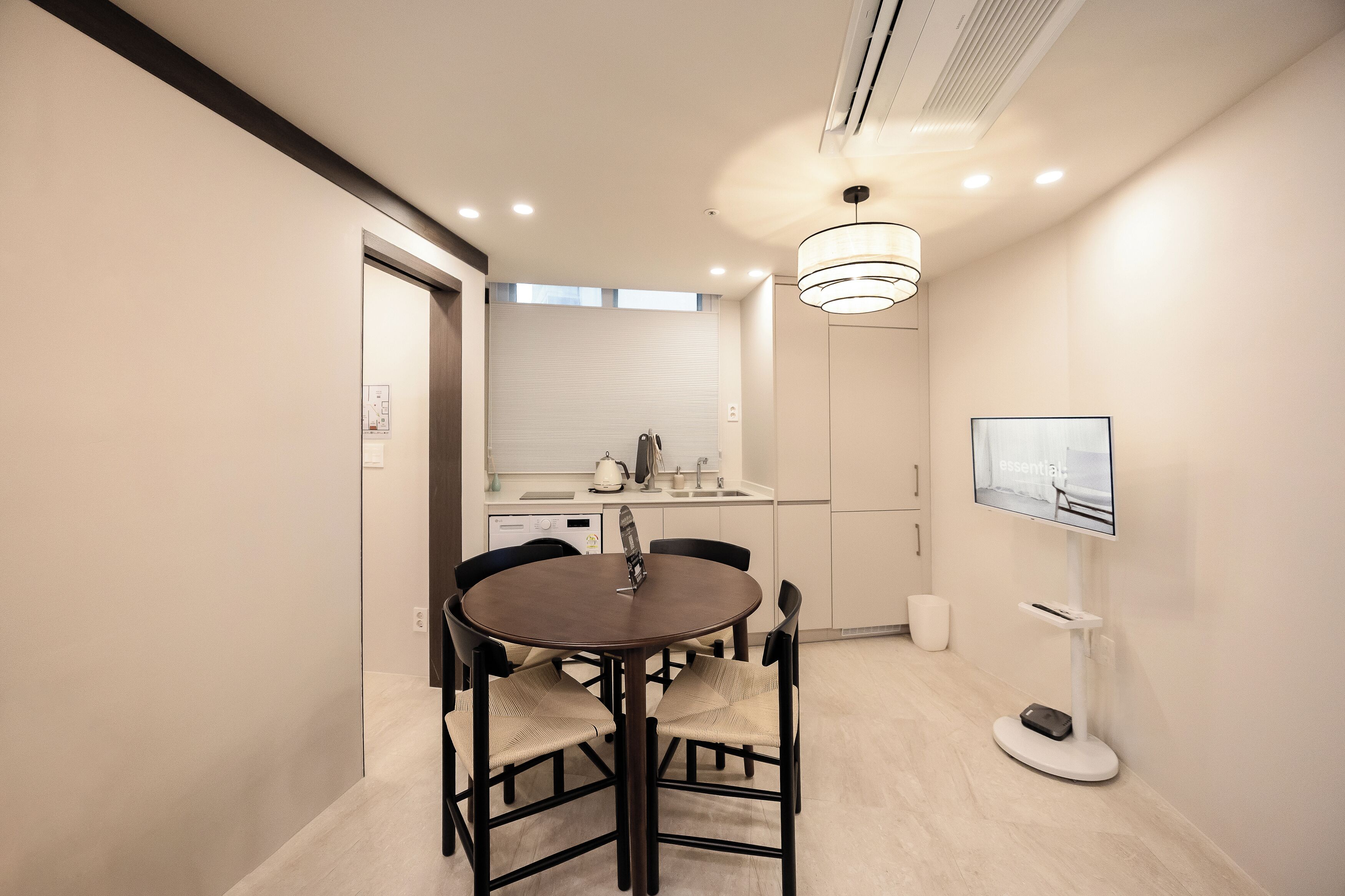 A modern kitchen with a dining table and chairs, a TV mounted on the wall, and a small window.