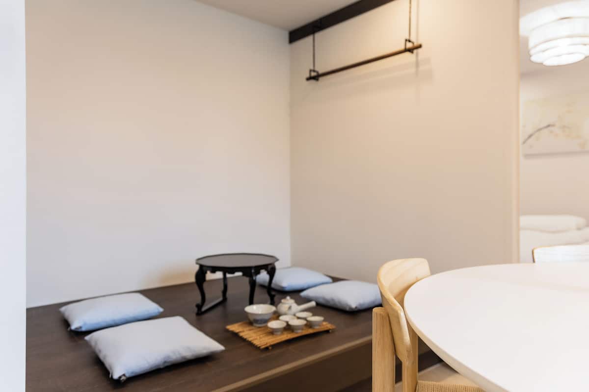 Une pièce au décor minimaliste, avec une table ronde, une petite table noire et plusieurs coussins.