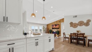 Una cucina moderna con mobili bianchi, illuminazione a sospensione e un'area pranzo con tavolo e sedie in legno.