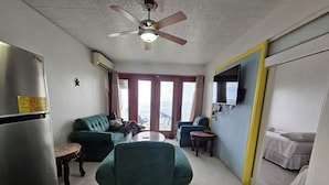 A living room with a sofa, a chair, a small table, a ceiling fan, a TV, and a bed. - Seaview Condo Ocho Rios with private access to Mahogany beach (Ocho Rios)