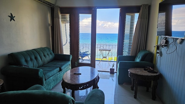 A living room with a green sofa, a round table, and a view of the ocean through large glass doors. - Seaview Condo Ocho Rios with private access to Mahogany beach (Ocho Rios)