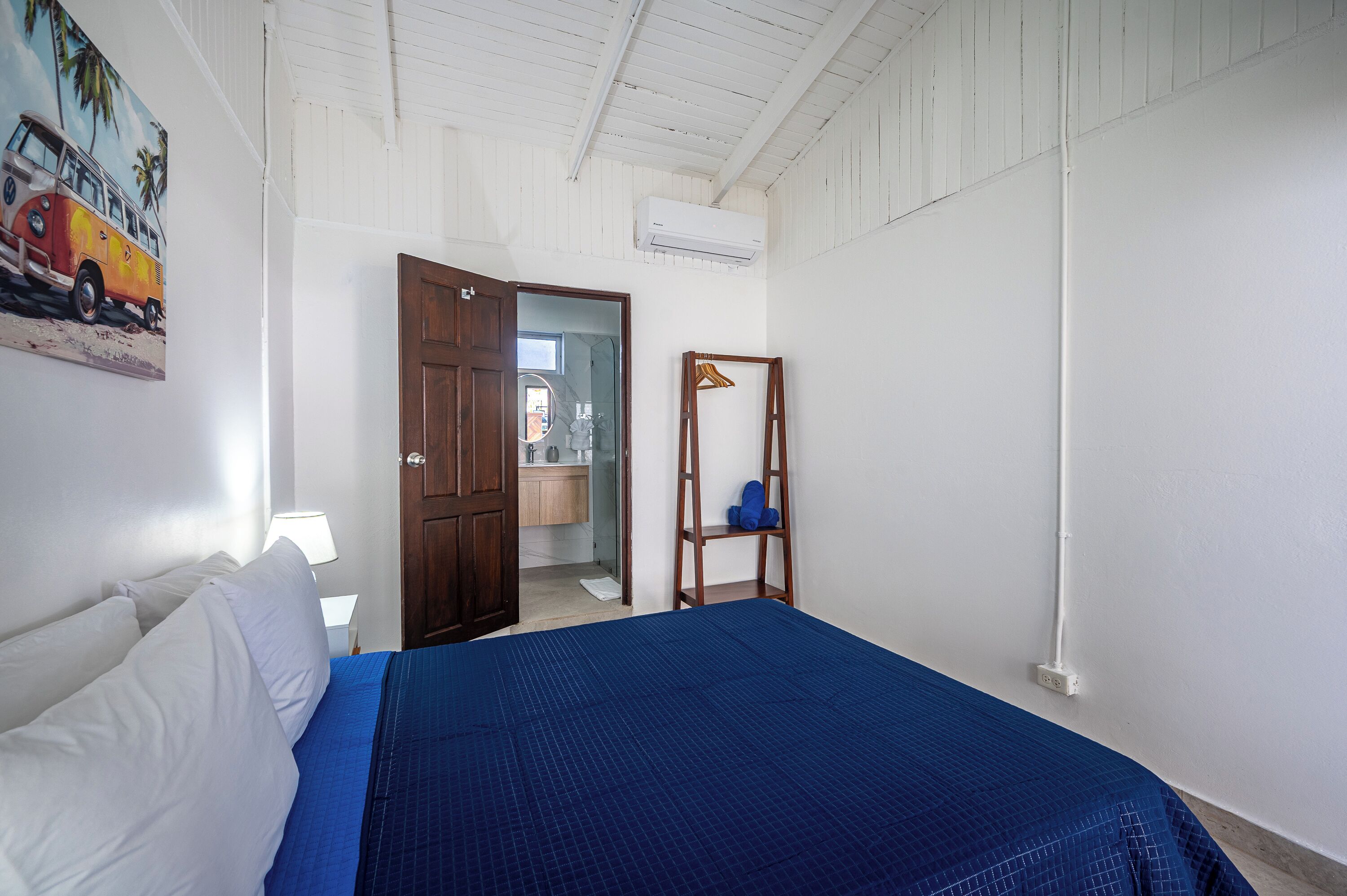 A bedroom with a bed, a wooden wardrobe, a mirror, and a door leading to a bathroom.