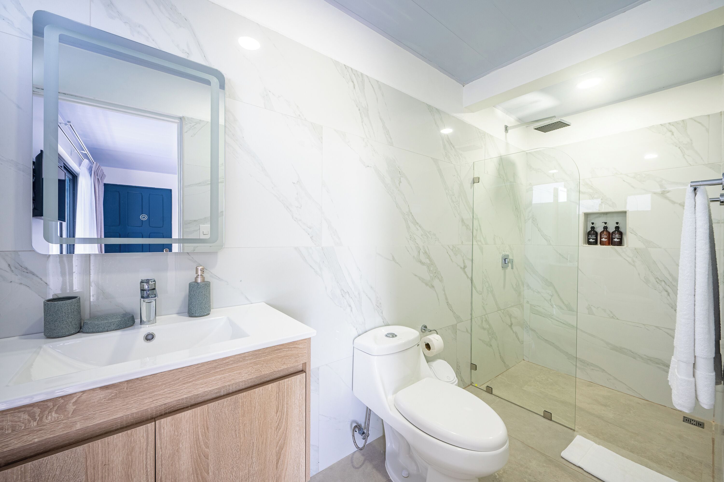 A modern bathroom with a marble wall, a glass shower enclosure, a white sink, and a toilet.