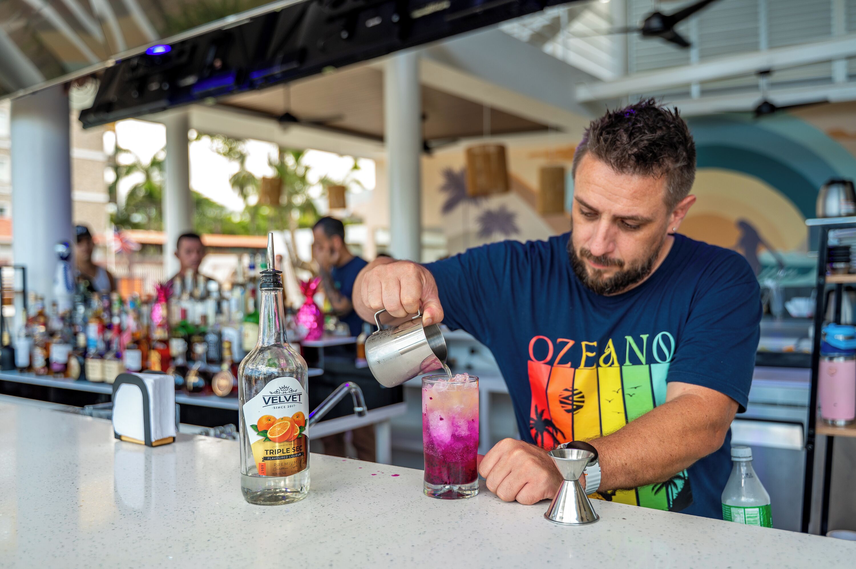 A bartender pouring a drink into a tall glass.