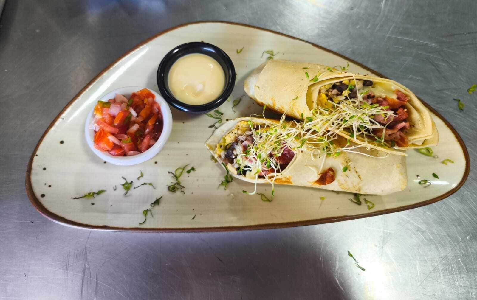 A plate with two wraps and a small bowl of salsa.