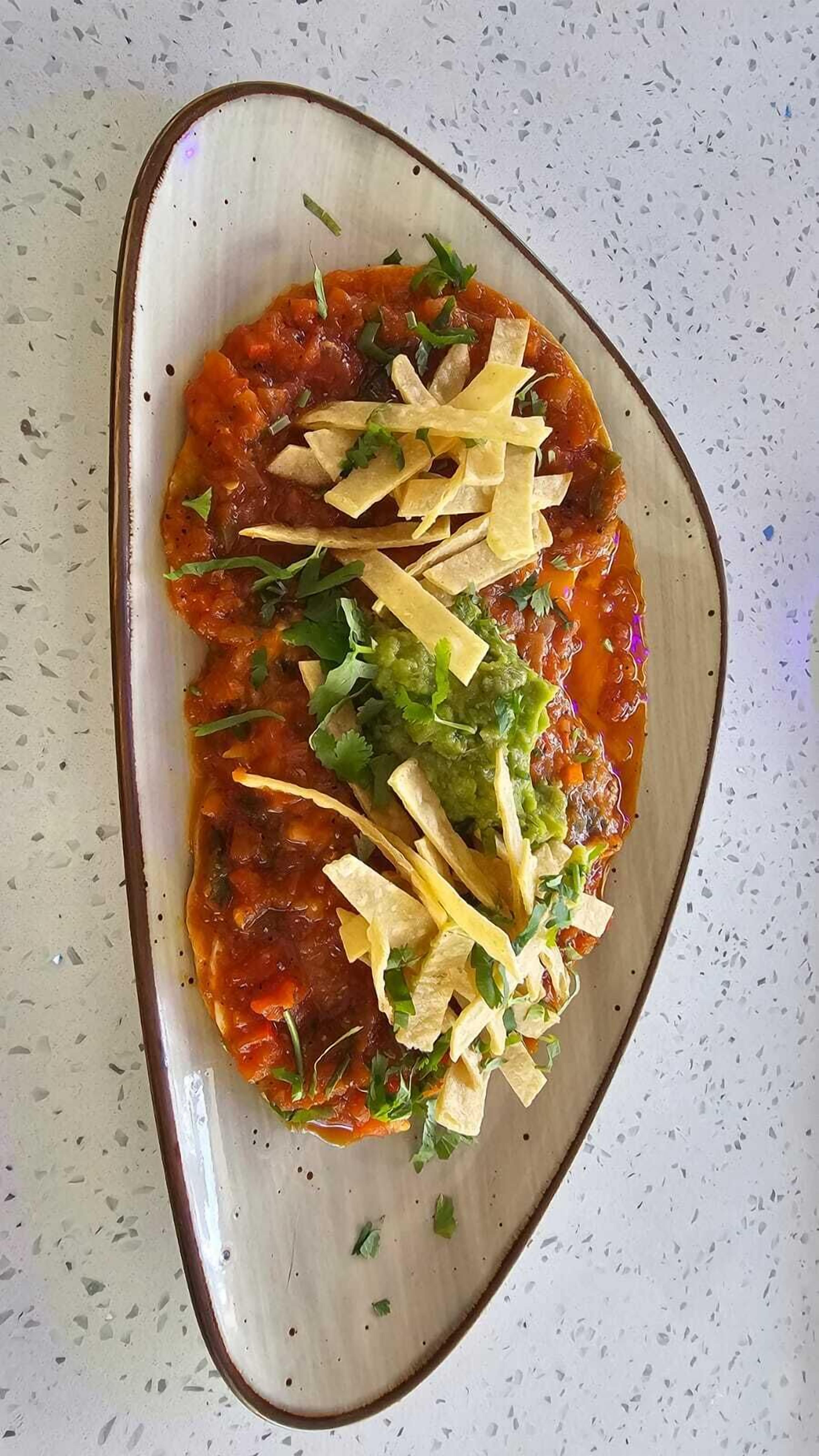 Un plato de enchiladas cubiertas de salsa, queso y cilantro.