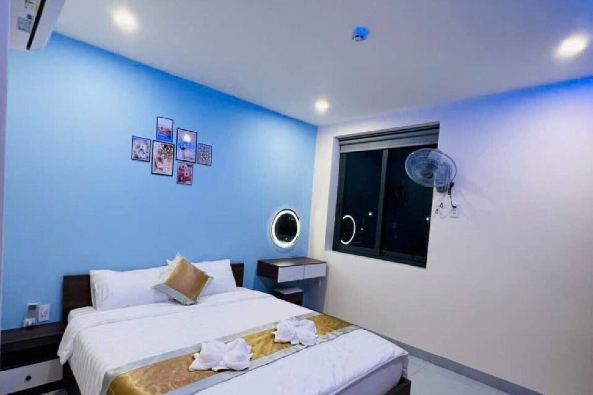 A modern hotel room with a large bed, a bedside table, a wall-mounted fan, and a window with a view.