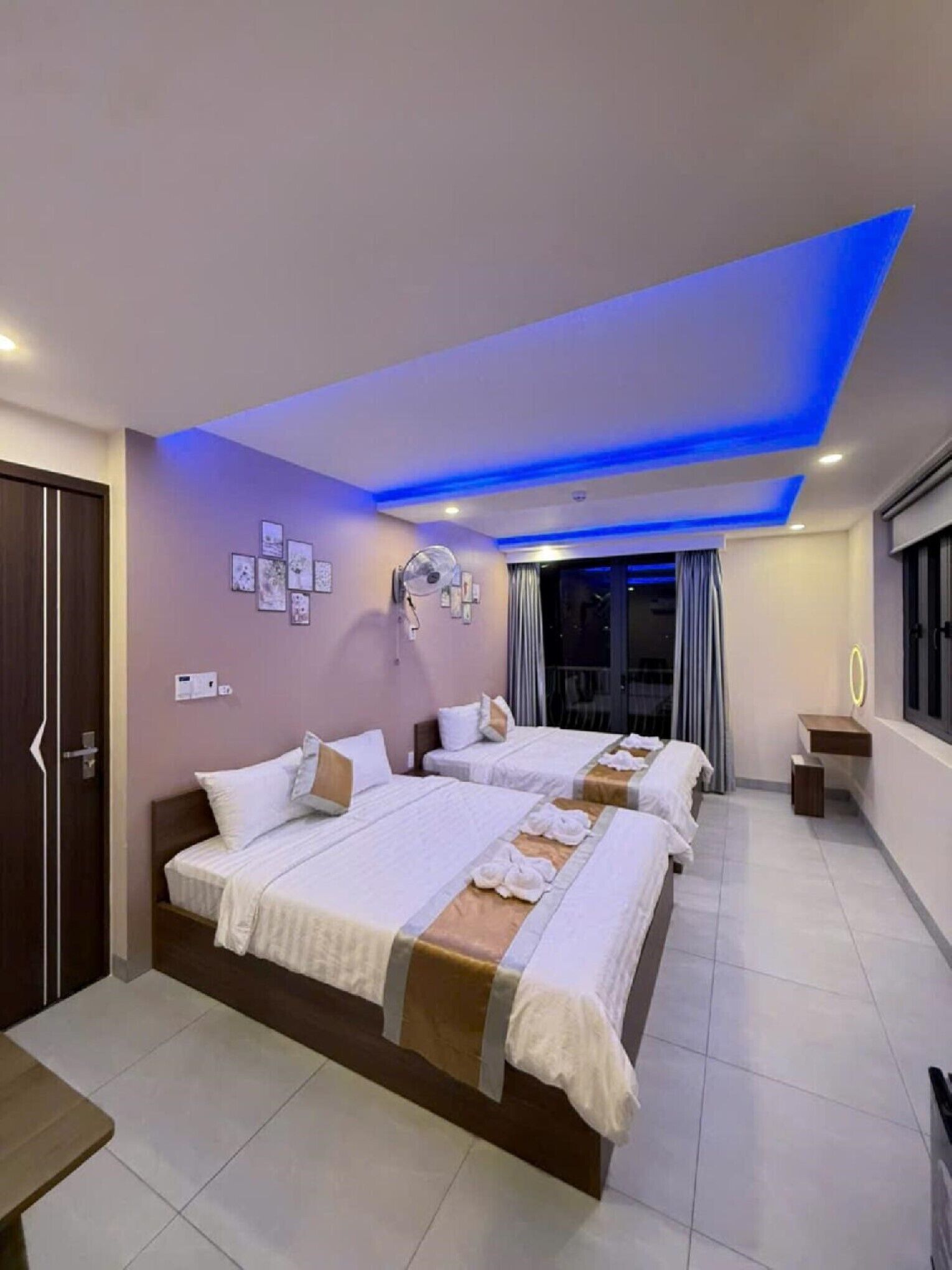 A hotel room with a large bed, bedside tables, a small desk, and a window with curtains.