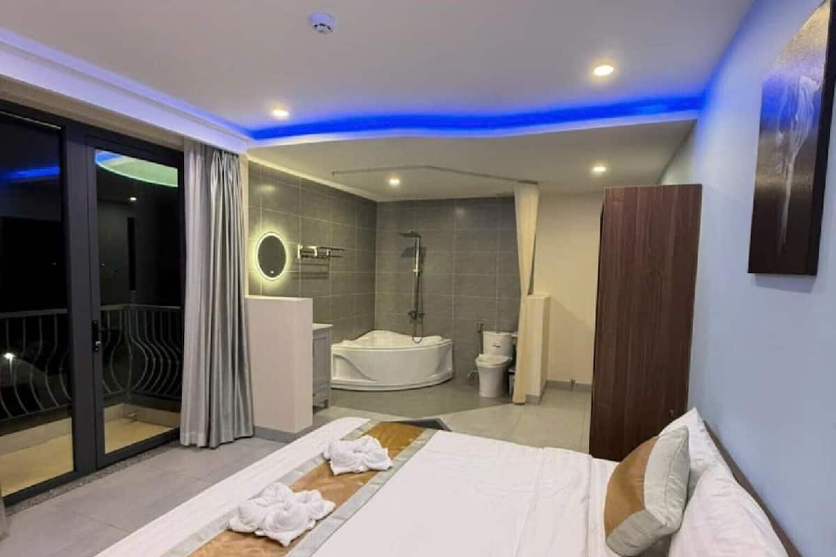 A modern hotel room with a large bed, a separate bathroom with a bathtub, and a balcony with a glass door.