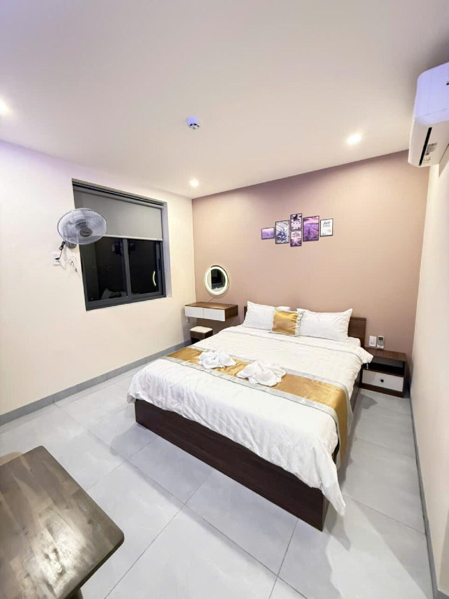A modern hotel room with a large bed, bedside tables, a round mirror, and a wall-mounted fan.