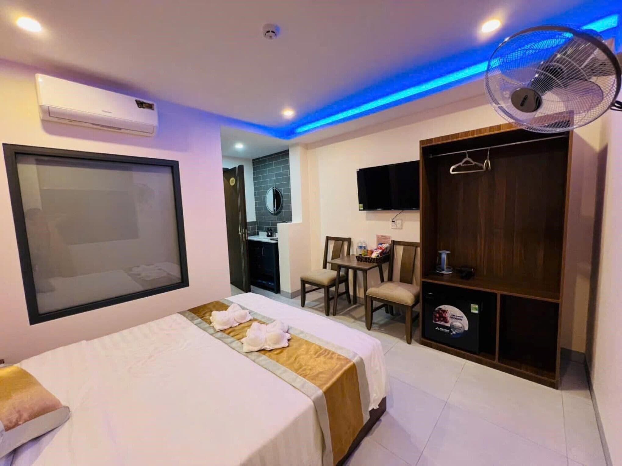 Ein Hotelzimmer mit Bett, Kleiderschrank, Schreibtisch mit Stühlen, Fernseher und Ventilator.