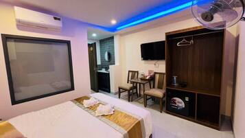 Ein Hotelzimmer mit Bett, Kleiderschrank, Schreibtisch mit Stühlen, Fernseher und Ventilator.