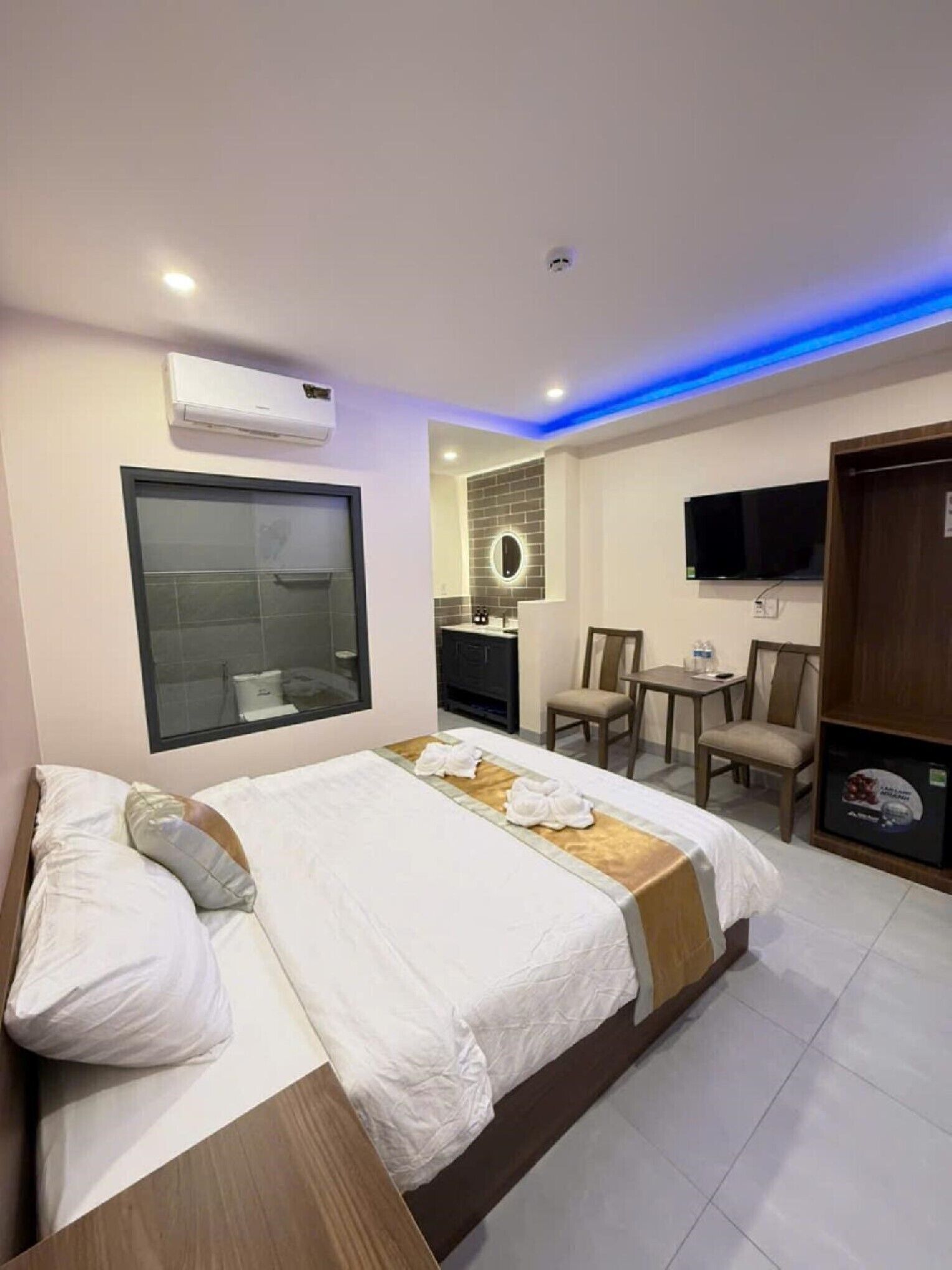 A hotel room with a bed, a desk, a chair, a TV, and an air conditioning unit.