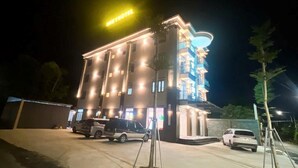 Un hotel de varios pisos con señalización iluminada y automóviles estacionados frente a él.
