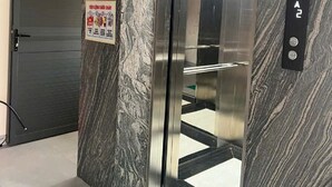 Un ascensor con una pared de mármol, una puerta con un letrero rojo y un felpudo verde que dice “BIENVENIDOS”.