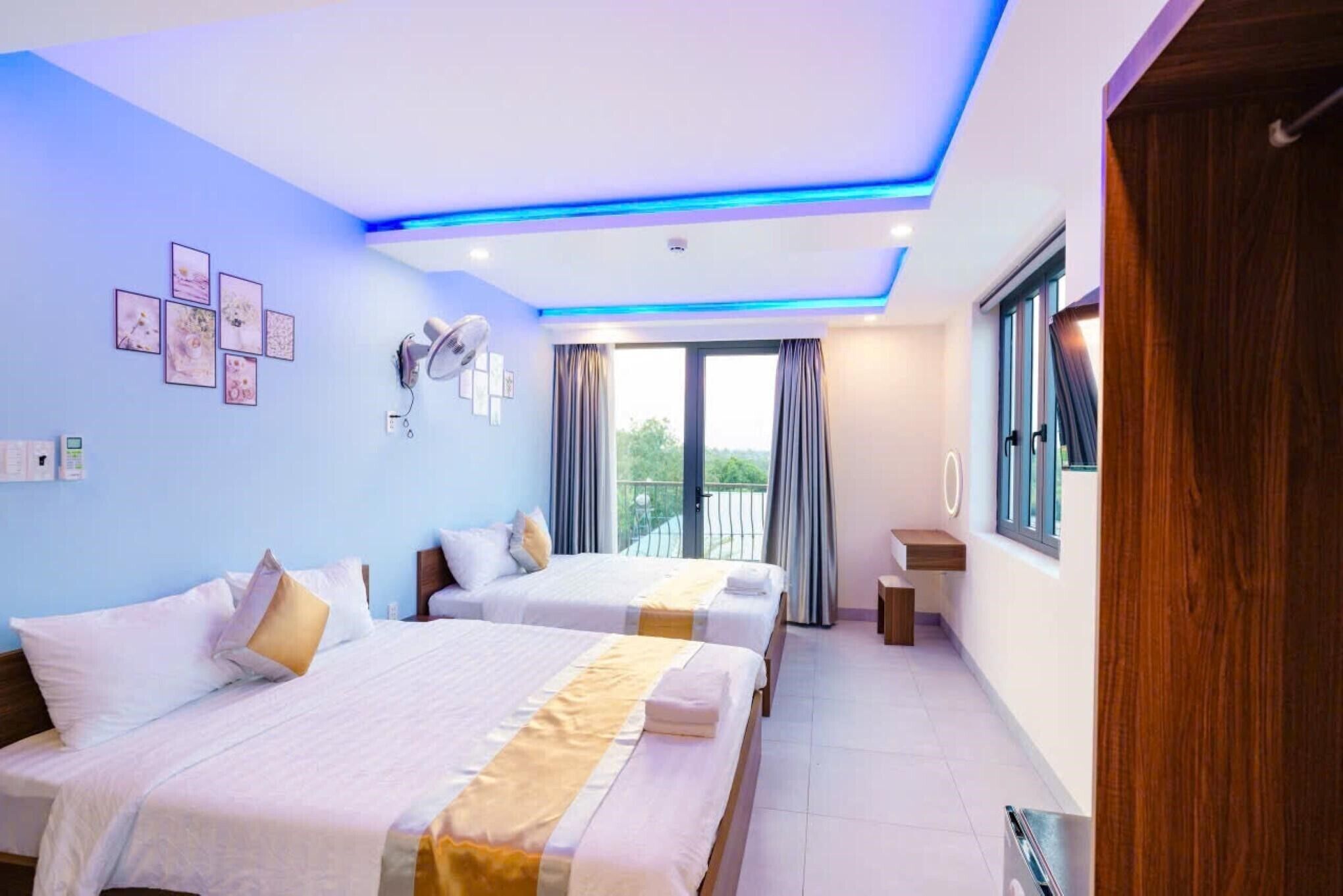 A hotel room with two beds, a ceiling fan, a window with curtains, and a balcony.