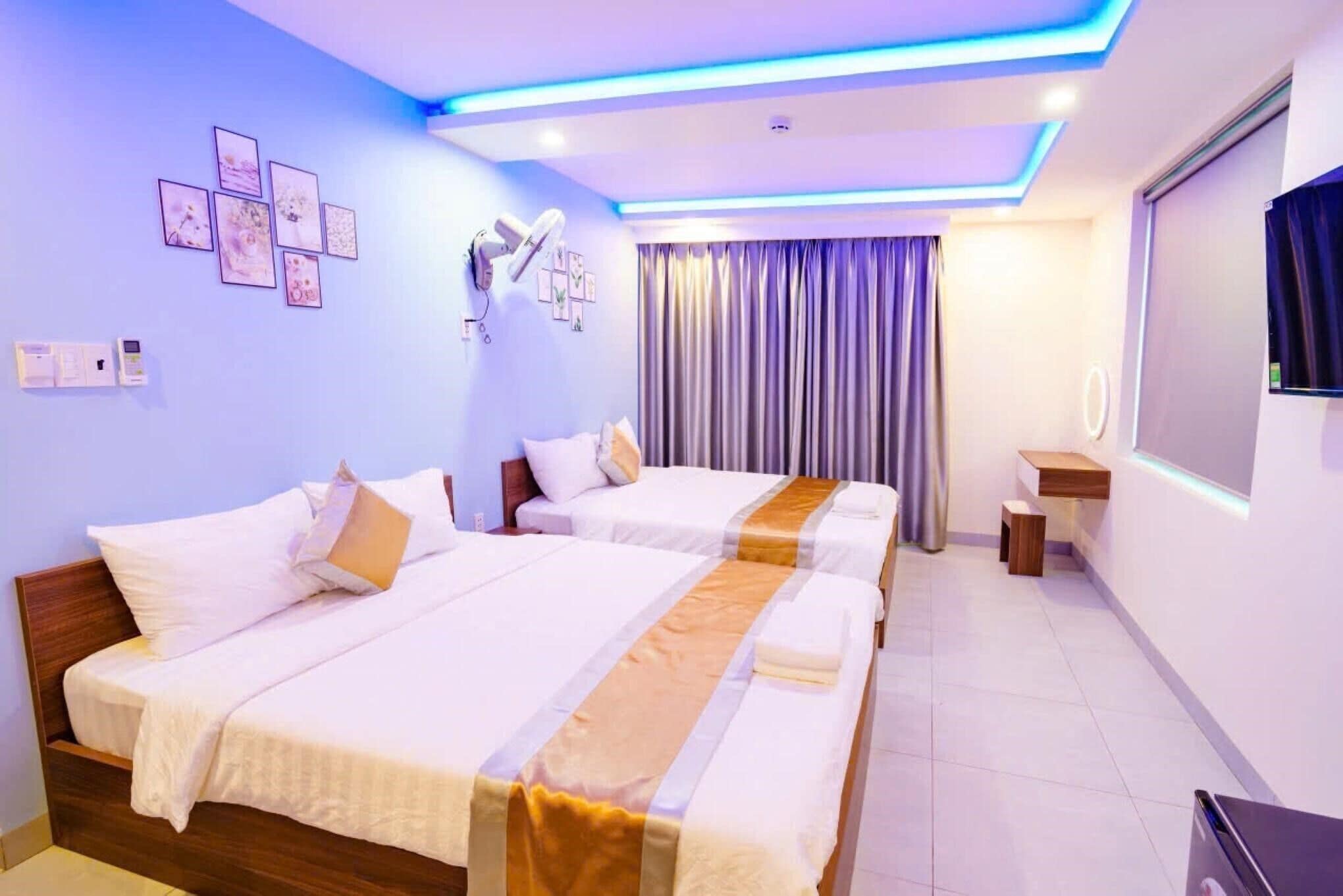 Habitación de hotel con dos camas, una lámpara en el techo, un televisor montado en la pared y una ventana con cortinas.