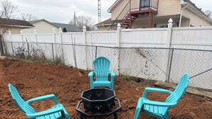 Un área de estar al aire libre con sillas turquesas y una mesa negra, rodeada por una cerca blanca y una cerca de malla metálica.