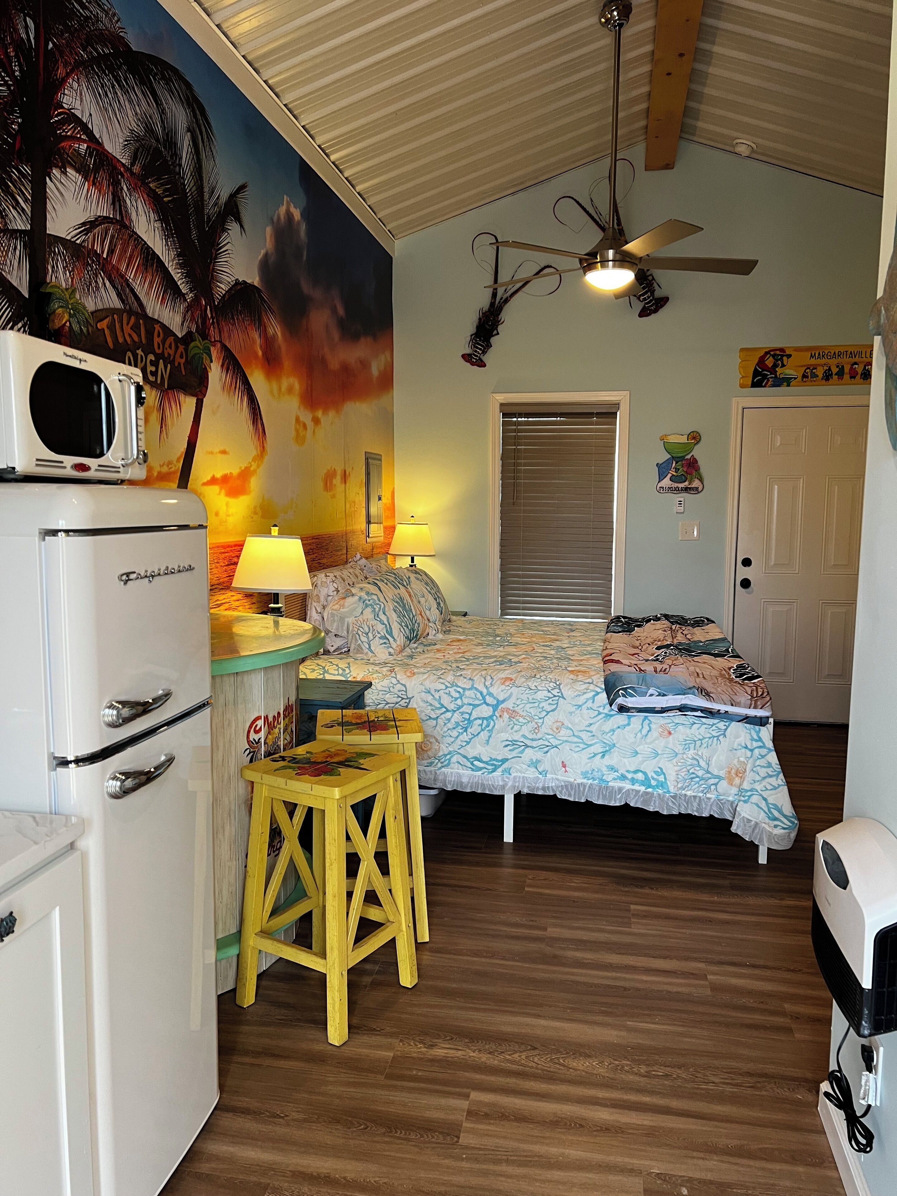 A room with a bed, a ceiling fan, a microwave, a small table, and a refrigerator.