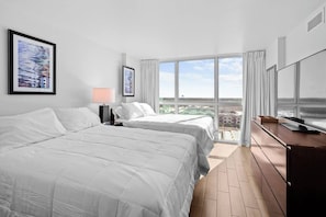 A hotel room with two beds, a desk, a TV, and large windows offering a city view. - Cozy Apartment | Near Downtown Fort Myers (Fort Myers)