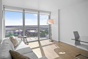 A modern living room with a large window, a glass table, a sofa, and a lamp. - Cozy Apartment | Near Downtown Fort Myers (Fort Myers)